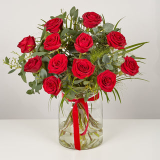 Bouquet of red roses in a clear vase with a red ribbon on a white background