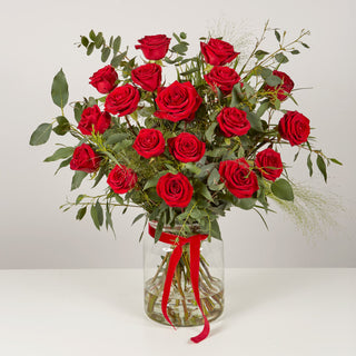 Bouquet of red roses in a clear vase with a red ribbon on a white background
