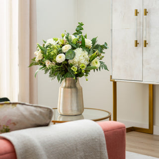 Bouquet of flowers in a vase on a table in a room with a pink chair and white cabinet.