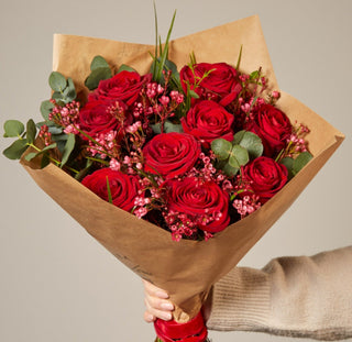 Bouquet of red roses wrapped in brown paper held by a person wearing a beige sweater.